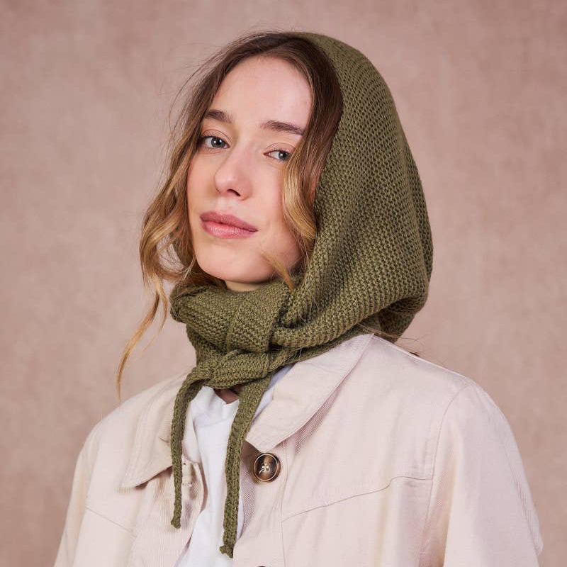 Woman wearing a green knitted hood and beige jacket against a pink background