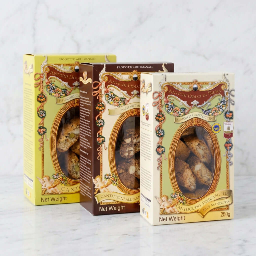 Three boxes of Anticoi Dolci di Siena Cannoli al Vapore by Anticoi, arranged in a fan shape on a white background. The packaging features traditional Italian designs with gold frames, cherubs, and illustrations, showing the baked cannoli inside through clear windows.