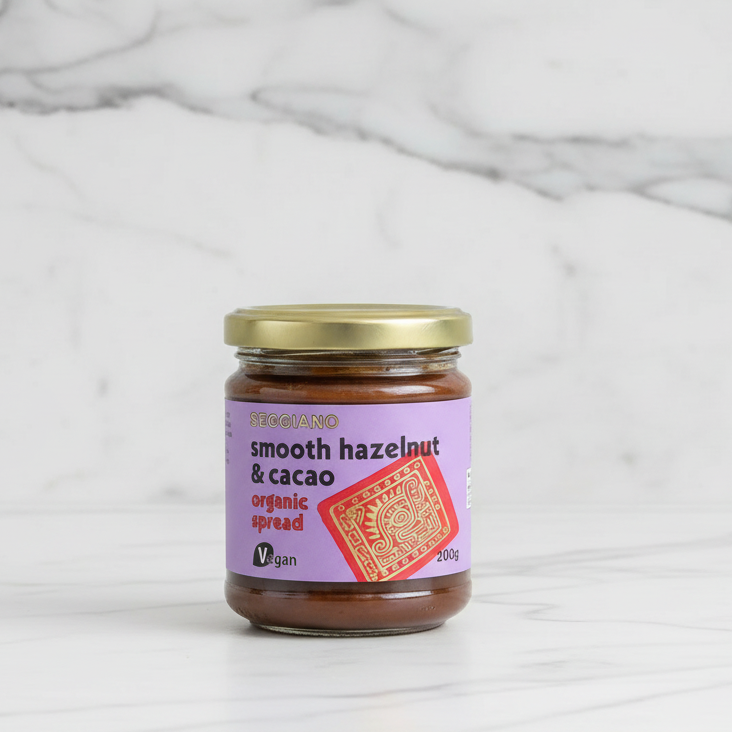 A jar of Seggiano Smooth Hazelnut & Cacao Organic Spread, 200g, with a purple label indicating it's vegan.