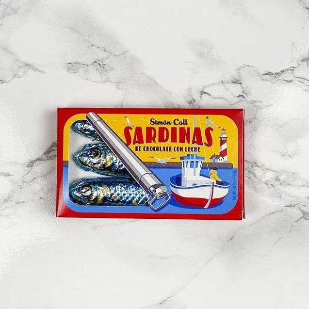 Milk chocolate sardines wrapped in aluminum foil, designed to look like a sardine can, placed on a marble surface.